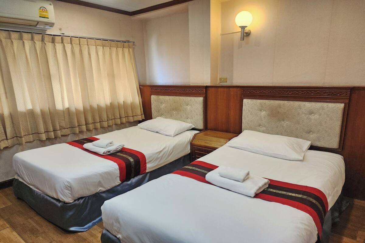 A hotel room with two single beds, a wooden headboard, a wall-mounted air conditioner, and a night light.