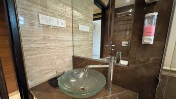 Un baño con un lavabo de vidrio, un grifo moderno y un dispensador de jabón.