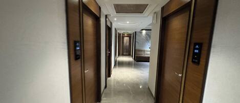 A modern hallway with marble flooring and wooden doors, leading to a room with a marble wall and a large mirror.