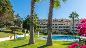 Une piscine entourée de palmiers, avec une bouée de sauvetage à proximité, et un bâtiment doté de nombreux balcons en arrière-plan.