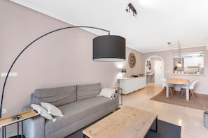 A modern living room with a grey sofa, a wooden coffee table, a black floor lamp, and a kitchen area in the background.