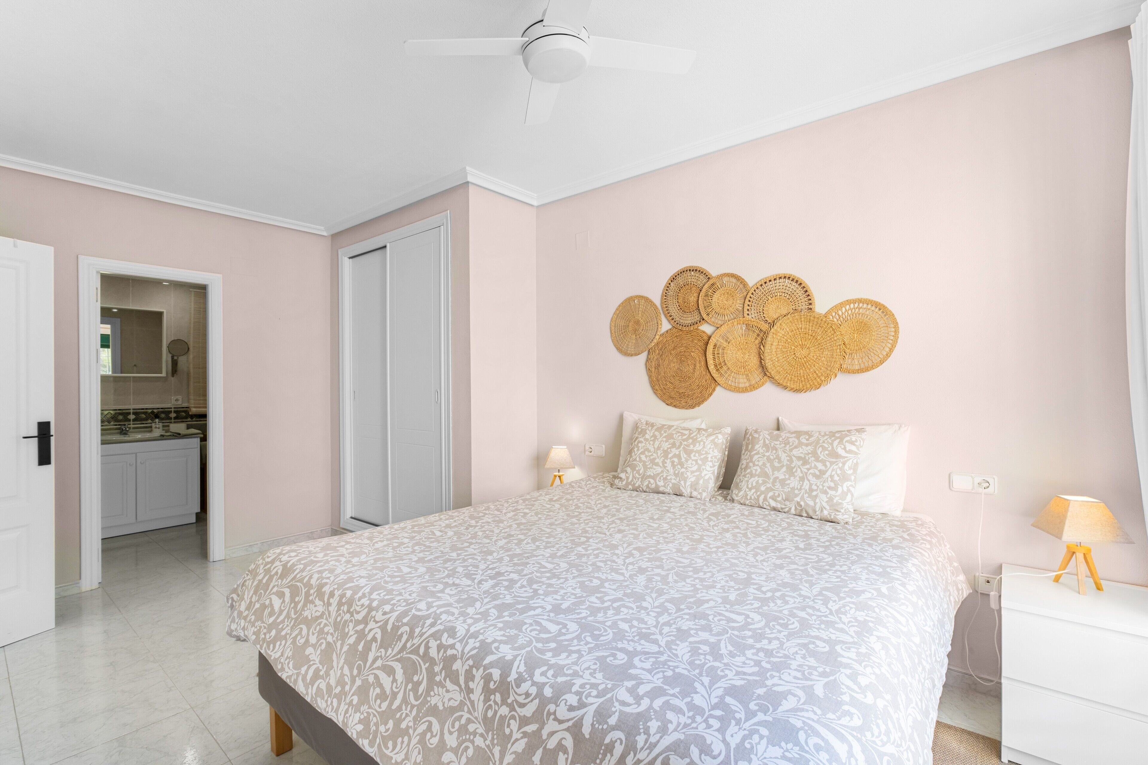 A bedroom with a bed, bedside lamps, a ceiling fan, and a wall with woven decorations.