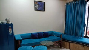 Una stanza con un divano blu, due poggiapiedi, un tavolino in vetro e un frigorifero.