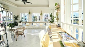 A bright, open-plan living area with a ceiling fan, large windows, and a variety of plants. - Sleepy Nomad Hostel (Malacca City)