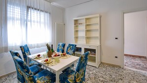 A dining area with a white table, blue floral chairs, and a white cabinet with shelves. - Lovely apartment in Chioggia with WiFi (Chioggia)