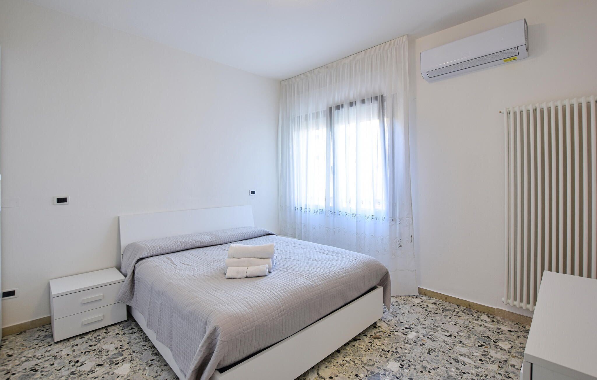 Une chambre à coucher avec un lit, une table de chevet, un radiateur et une fenêtre avec des rideaux.