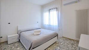 A bedroom with a bed, a nightstand, a radiator, and a window with curtains. - Lovely apartment in Chioggia with WiFi (Chioggia)