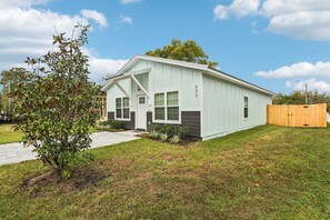 A single-story house with a light green exterior, a front porch, and a fenced backyard. - 3 Homes IN A ROW! | 30 People | Firepits & Yards (St. Augustine)