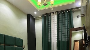 Un lit bien fait, avec une literie blanche, dans une pièce aux rideaux verts et dotée d’un grand miroir.