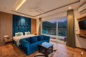 Un dormitorio moderno con una cama grande, un sofá azul, una mesita pequeña y vistas a un bosque a través de un ventanal amplio.