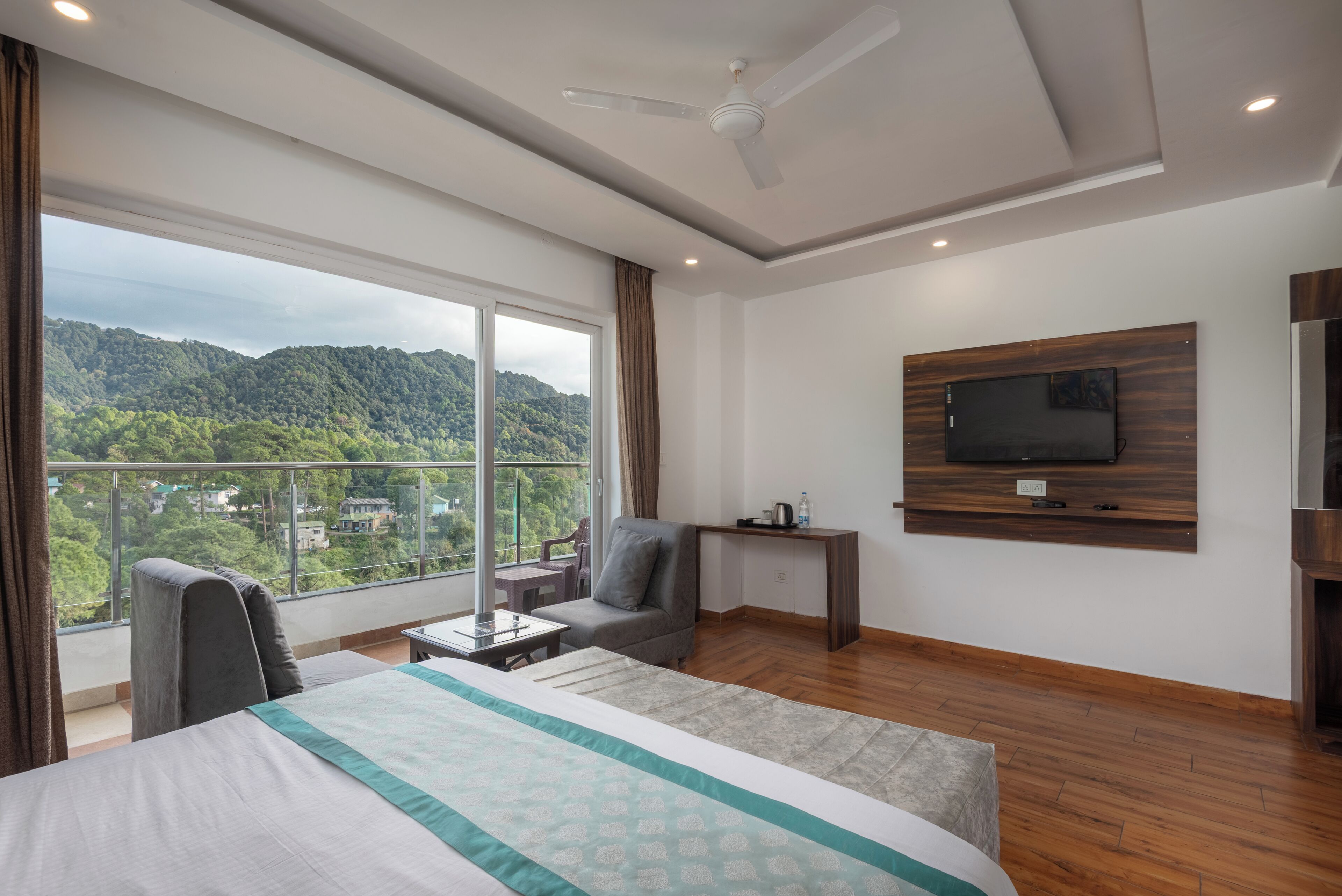 Habitación de hotel con cama, escritorio, silla, televisor en la pared y vista a un paisaje montañoso.