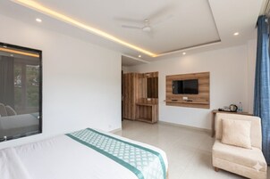 Un cuarto de hotel moderno con una cama, un televisor montado en la pared, un ventilador de techo y vistas al exterior a través de una ventana.