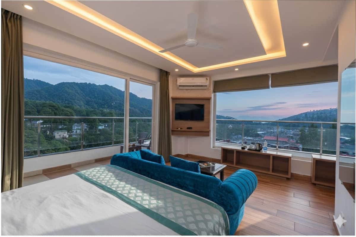 A hotel room with a large bed, a sofa, a TV, and a balcony with a city view.