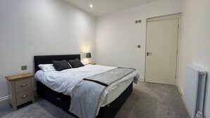 Ein Schlafzimmer mit Bett, Nachttisch, Lampe und einer Tür.