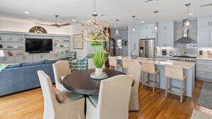 Een moderne keuken met een centraal eiland, een zithoek met een ronde tafel, en een woonkamer met een bank en televisie.