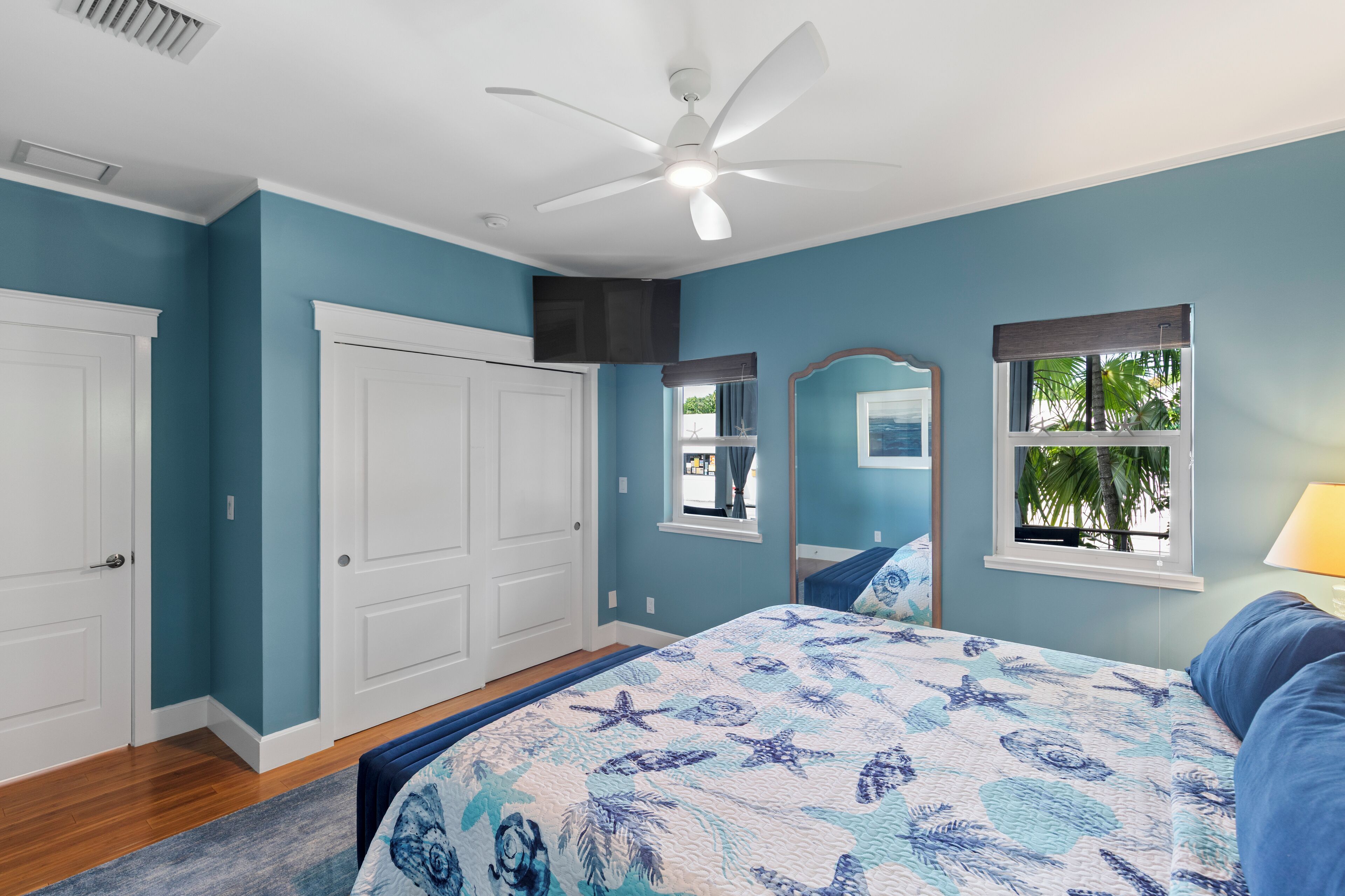 A bedroom with a bed, a ceiling fan, a window with a view, and a door.