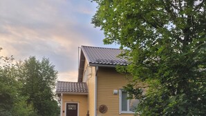 Une maison jaune avec un toit en tuiles, un porche à l’avant et un climatiseur.
