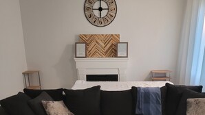 Un salon moderne avec un canapé d’angle noir, une table basse en bois et une cheminée dont le manteau est orné d’un motif en chevrons.