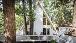 A white wooden cabin with a triangular roof, surrounded by tall trees.