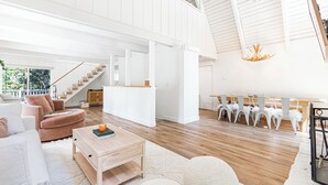 A spacious living area with a wooden floor, white furniture, and a staircase leading to an upper level.