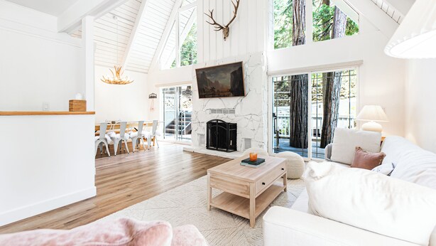 A spacious living room with a fireplace, a television mounted on the wall, and a large window offering a view of the outdoors.