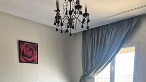 A bedroom with a tufted headboard, a large window with curtains, and a chandelier. - Luxurious sea view (Sousse)