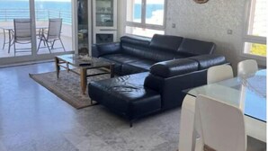 A spacious living room with a black leather sofa, a glass dining table, and a view of the ocean. - Luxurious sea view (Sousse)