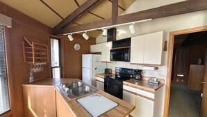 A compact kitchen with a sink, stove, microwave, and white cabinets. - Eagle River Northwoods Retreat - 3 Bedrooms - 2 Bathrooms (Eagle River)