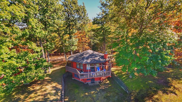 A red cabin with a balcony, surrounded by trees and a grassy area. - Eagle River Northwoods Retreat - 3 Bedrooms - 2 Bathrooms (Eagle River)