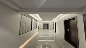 A modern hallway with a marble floor, framed artwork on the walls, and a dark wooden door at the end. - Hotel Star Square (Indore)