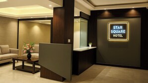 A hotel reception area with a modern design, including a reception desk, a sofa, and a wall-mounted sign for the Star Square Hotel. - Hotel Star Square (Indore)