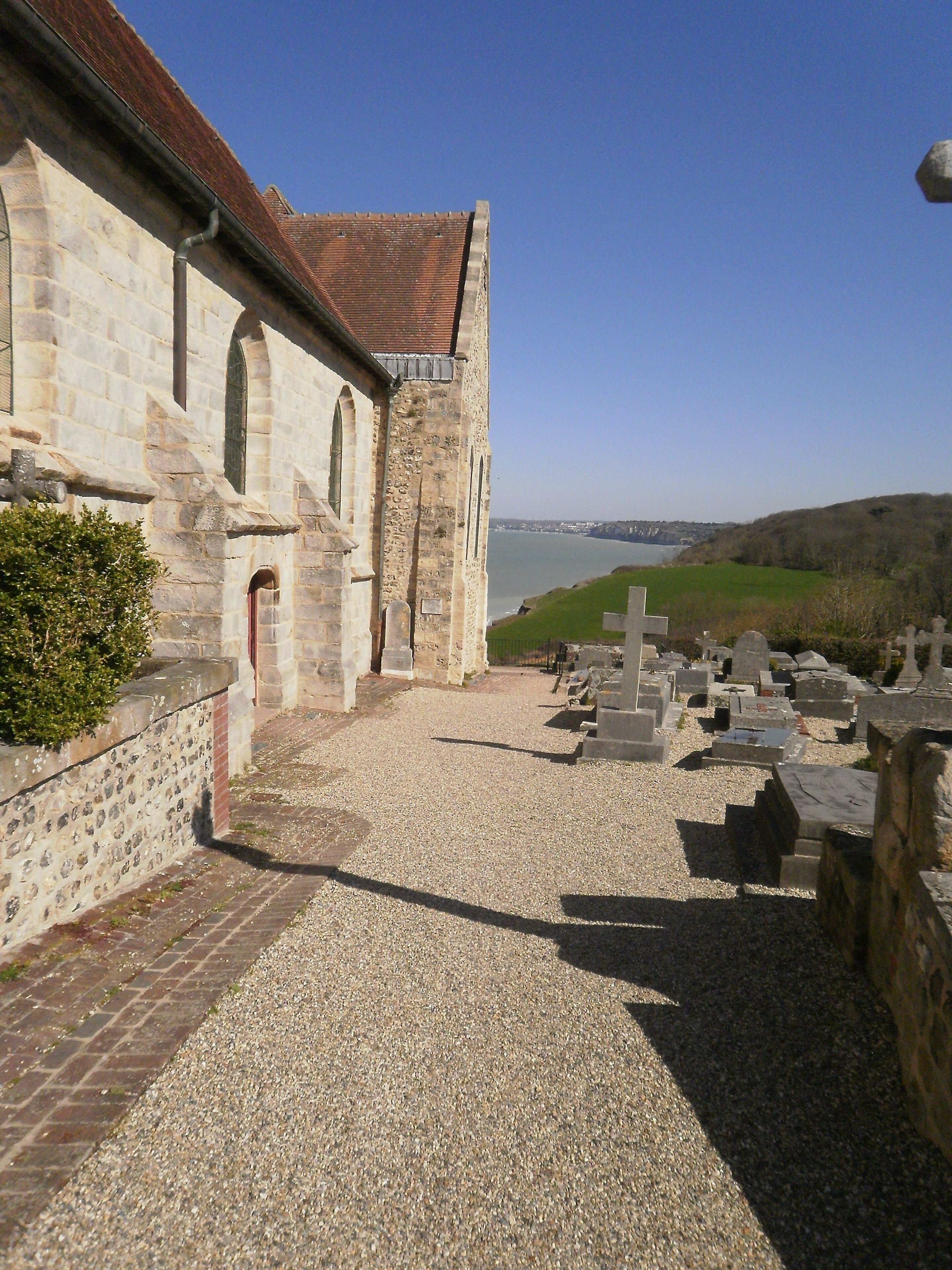 Un edificio histórico de piedra con un patio de grava y vista al mar.