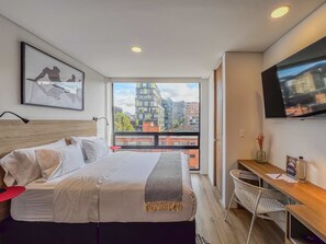 A modern bedroom with a large bed, a desk, and a TV.
