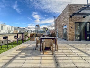 An outdoor patio with a table and chairs, a brick wall, and a view of the cityscape.