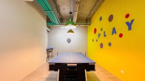 Une table de ping-pong dans une pièce avec un mur jaune et un jeu de fléchettes.
