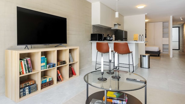 Ein modernes Wohnzimmer mit Flachbildfernseher, Bücherregal, Glastisch und einer Küche im Hintergrund.
