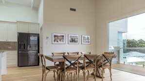 Une cuisine moderne avec un réfrigérateur en acier inoxydable, une table à manger en bois avec des chaises et des tableaux encadrés accrochés au mur.