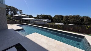 Une piscine rectangulaire à l’eau d’un bleu limpide, entourée d’une clôture noire et d’une terrasse dallée.