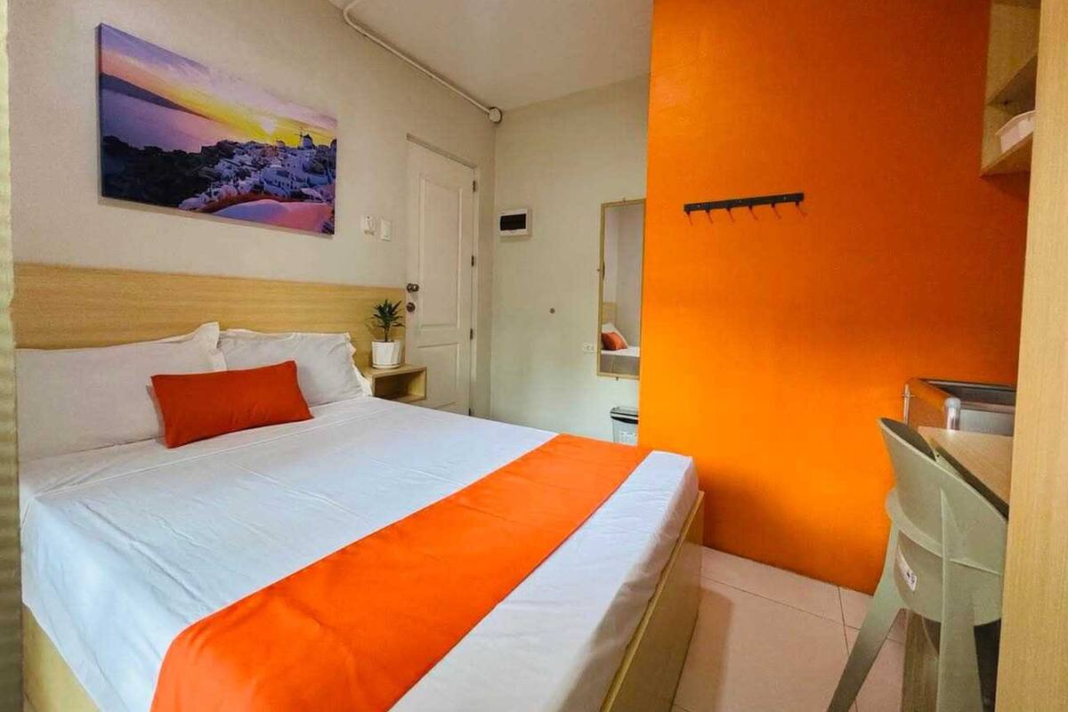 Een hotelkamer met een bed, nachtkastje, spiegel en een schilderij aan de muur.