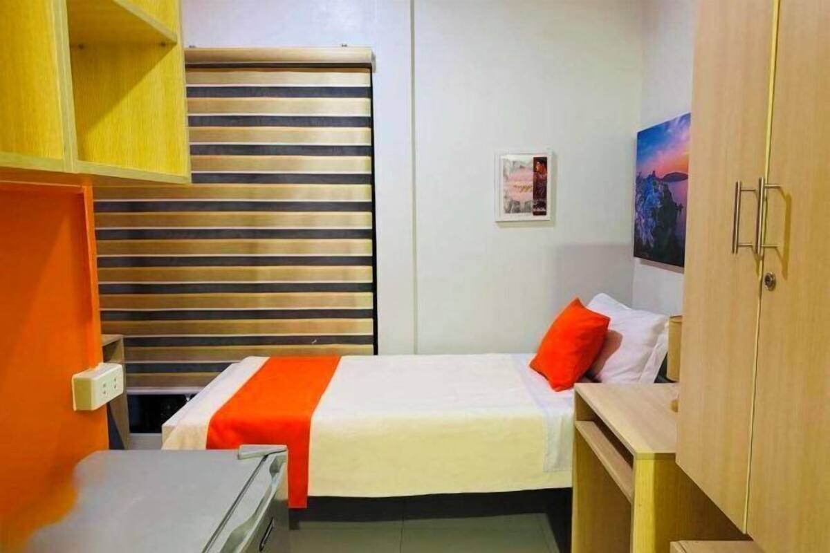 Een hotelkamer met een bed, een bureau, een kledingkast en een raam met jaloezieën.