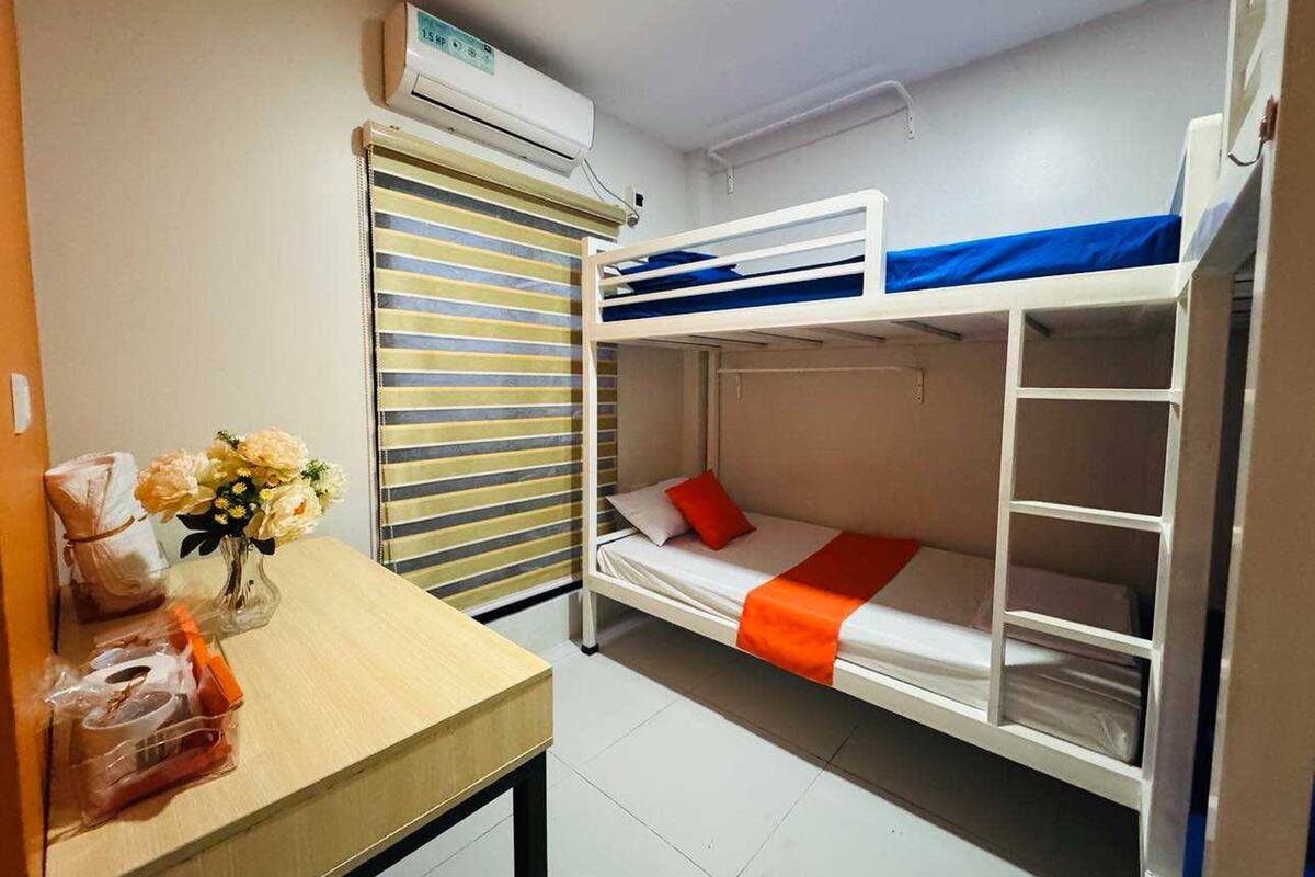 Een slaapkamer met stapelbed, een tafel, een raam met zonwering en een airconditioning.