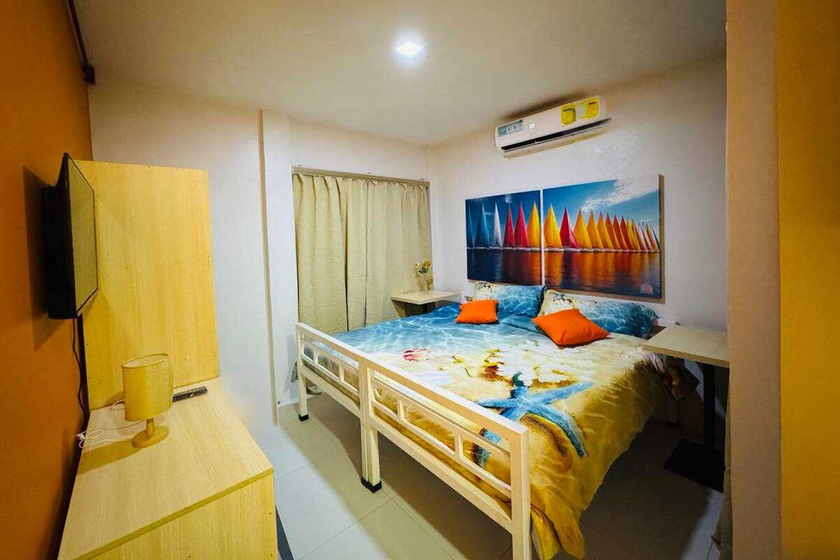 Een slaapkamer met een bed, een televisie, een bureau en een schilderij.
