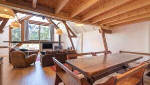 Un vaste espace de vie comprenant une table à manger en bois, des bancs, des canapés et une grande fenêtre donnant sur les montagnes.