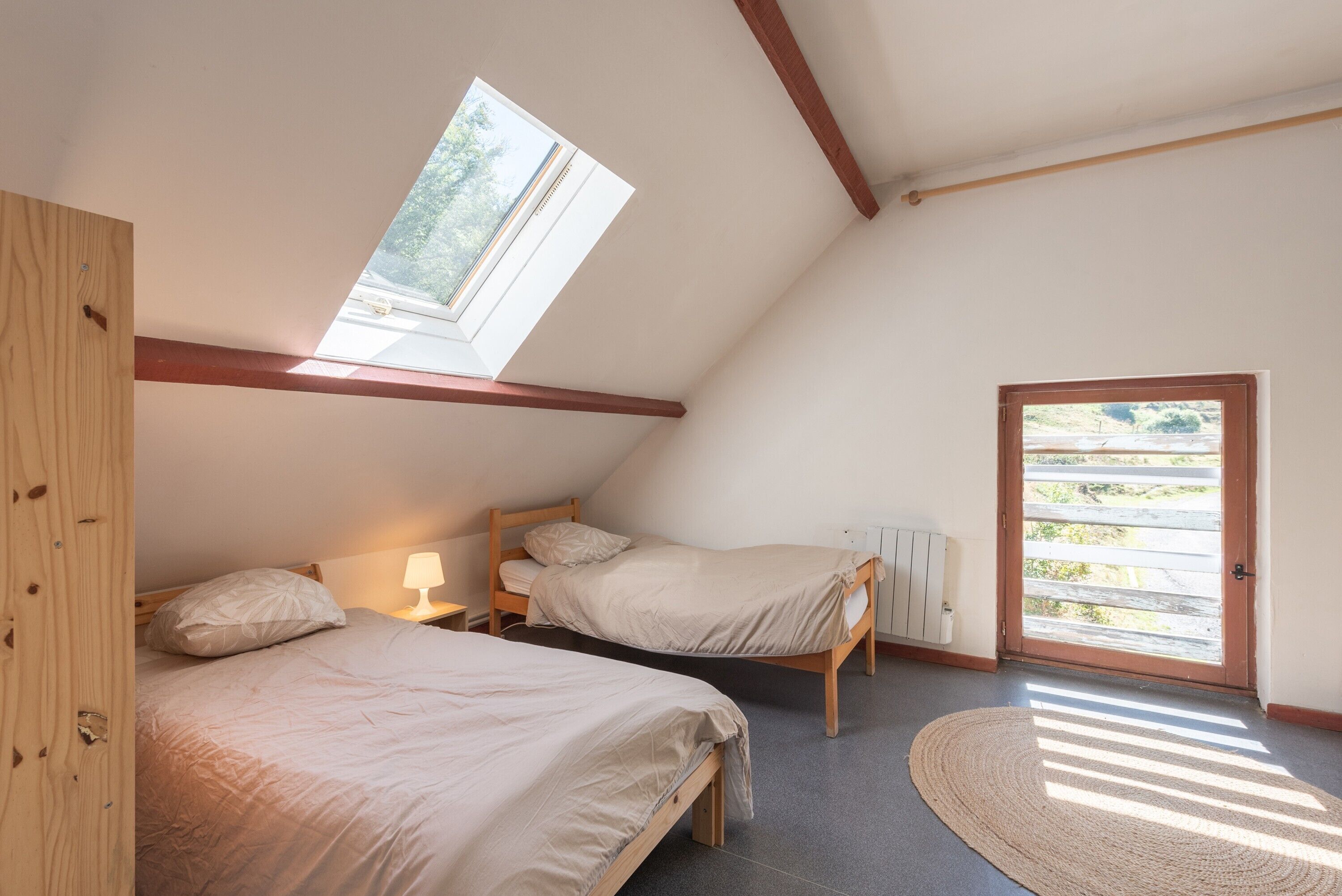 Ein Schlafzimmer mit zwei Betten, einem Oberlicht, einer Holztür und Blick ins Freie.
