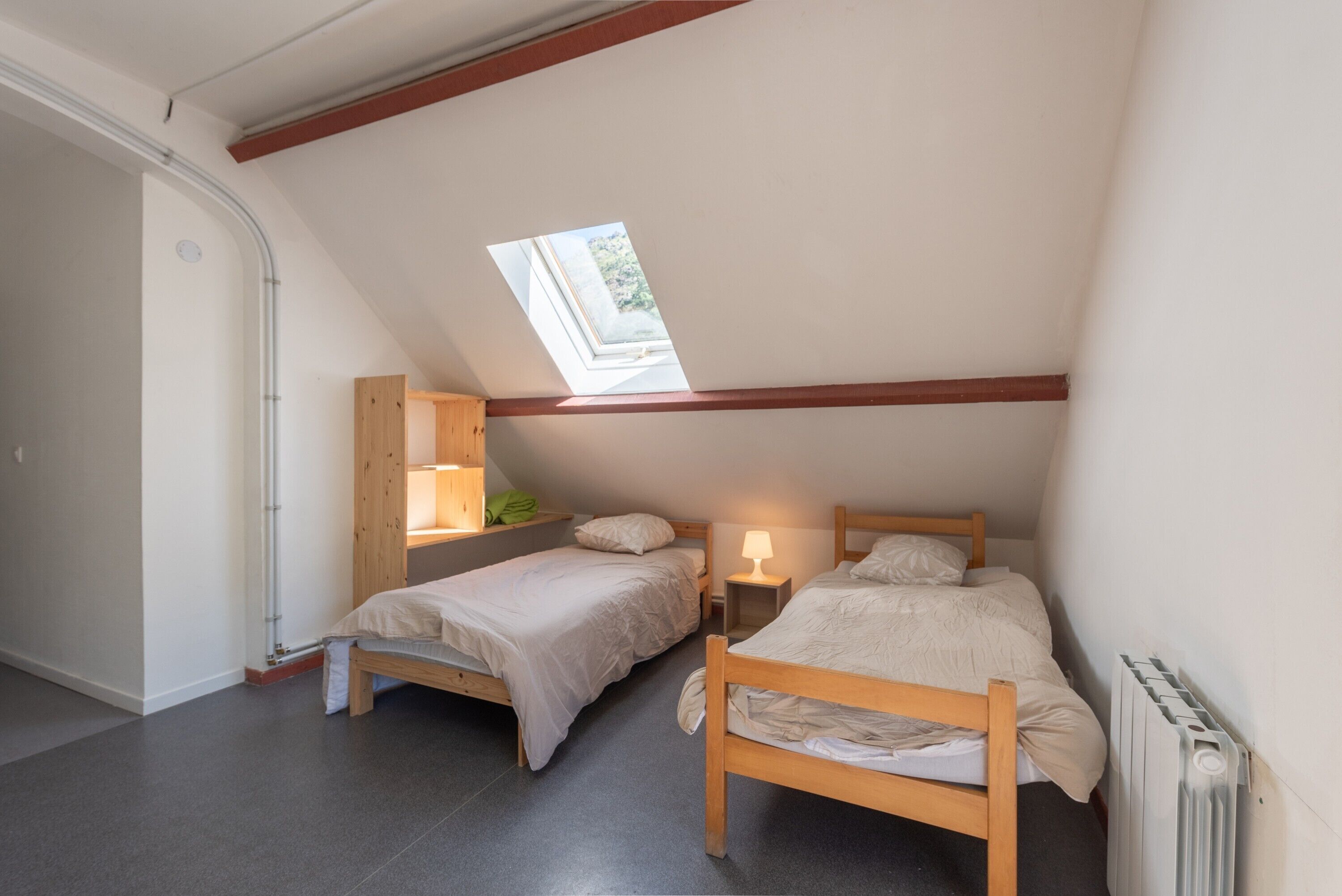 Una habitación pequeña y acogedora con dos camas de madera, un tragaluz, un radiador y un armario de madera.