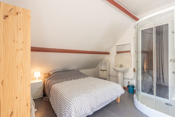 Un dormitorio con cama, mesita de noche, lámpara y zona de ducha con mampara de cristal.