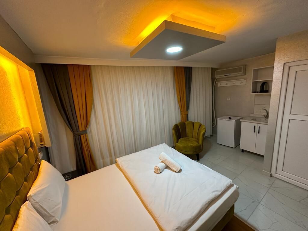 A hotel room with a bed, a chair, a kitchenette, and curtains.