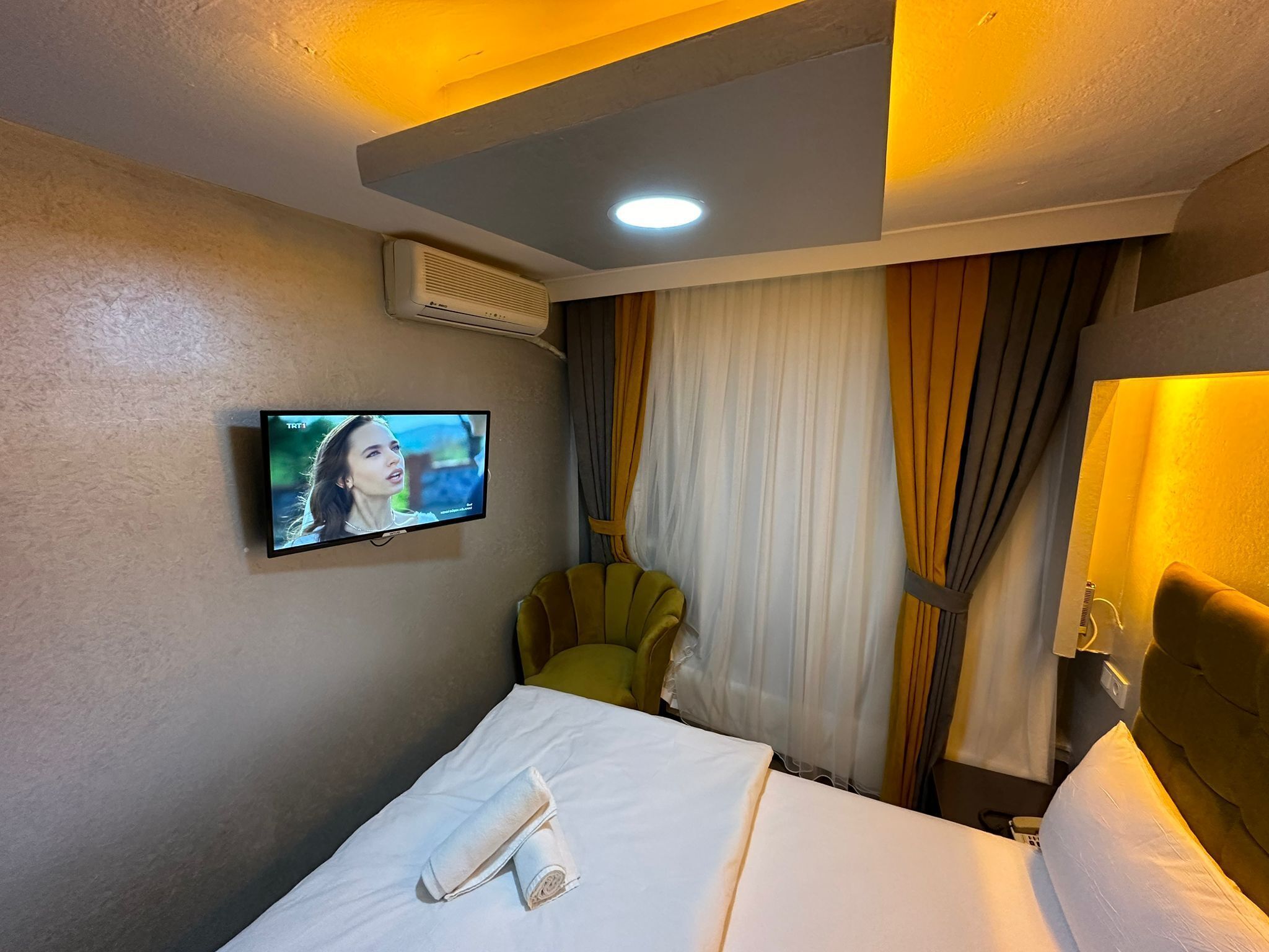 Una habitación de hotel con una cama, televisor montado en la pared, ventana con cortinas y aire acondicionado.
