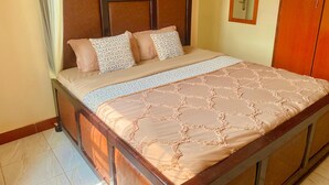 Een net opgemaakt bed met een bedspreidek en kussens, een houten hoofdbord met een spiegel en een houten garderobe.