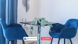 Ein modernes Wohnzimmer mit einem dunkelholznen Tisch, zwei blauen Stühlen, einem Topf mit Pflanze und einem Wandbild.